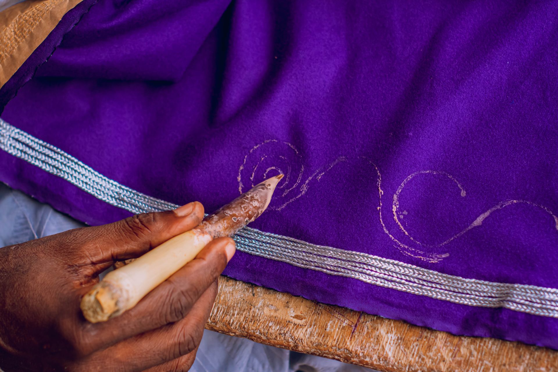 Close-up of artisan hand using a tool to decorate purple fabric with intricate patterns.