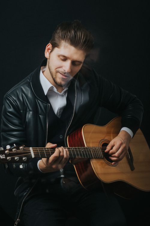 Free Young man in leather jacket playing acoustic guitar passionately. Stock Photo