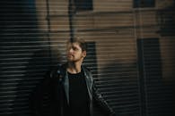 一名时尚男子身穿黑色皮夹克，在户外摆出沉思的姿势