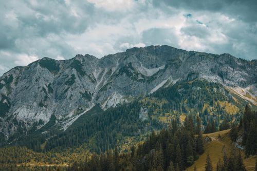 Free Serene view of rugged mountain peaks surrounded by lush forests under a cloudy sky. Stock Photo