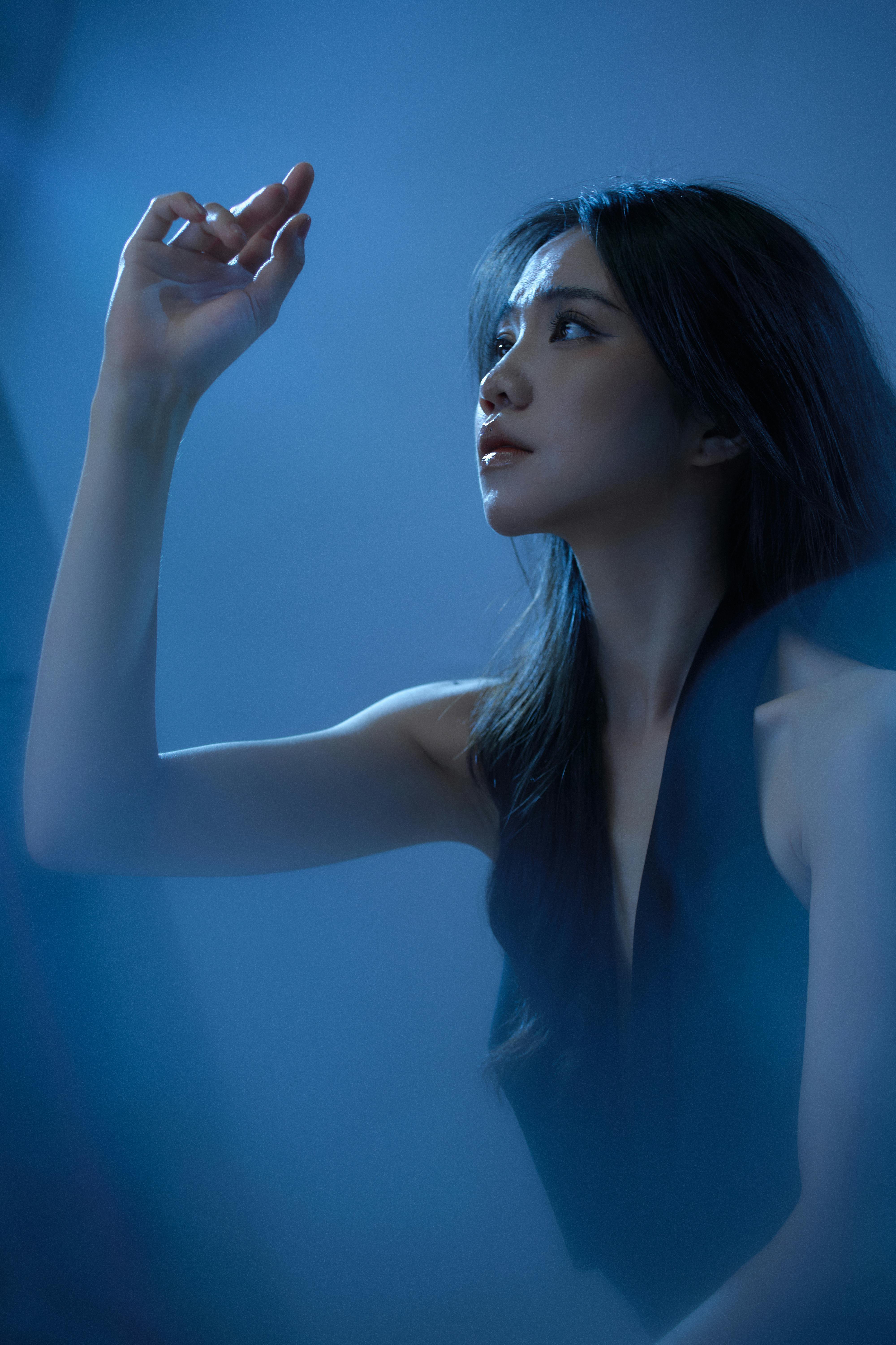 Elegant woman portrait bathed in dreamy soft blue light, serene and entranced expression in bedroom