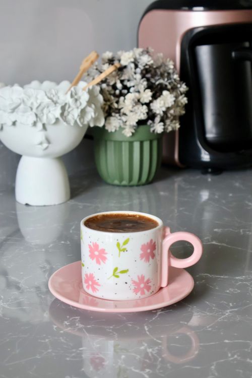Free Pink floral coffee cup on marble counter with flowers and coffee maker in background. Stock Photo