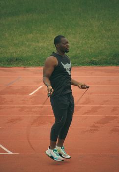 Athletic man exercises by jumping rope on a track during the day.