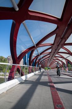 A cyclist rides on the striking red Peace Bridge in Calgary, Alberta, under a clear blue sky.