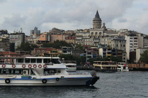Free View of Istanbul's iconic Galata Tower with ferries on the Bosphorus, highlighting urban life. Stock Photo