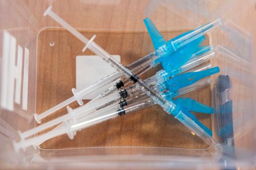 Free Top view of multiple disposable syringes inside a transparent medical container on a wooden surface. Stock Photo