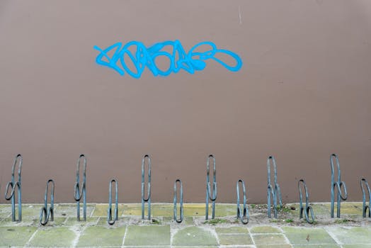 An empty bicycle rack with blue graffiti on a brown wall, creating urban texture.