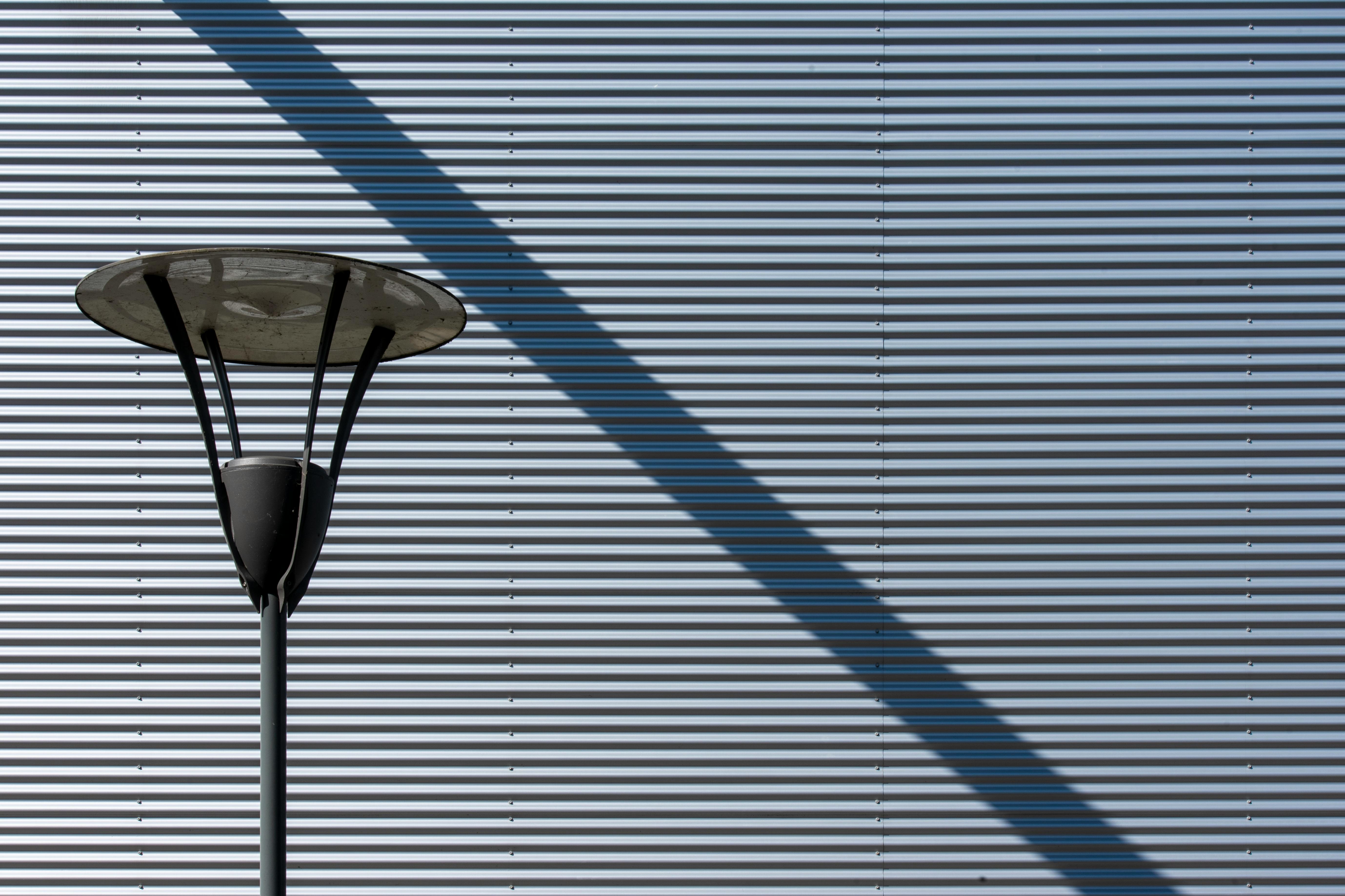 gratis Een straatlantaarn werpt een schaduw op een gegolfde metalen muur, waardoor lijnen en geometrie worden benadrukt. Stockfoto