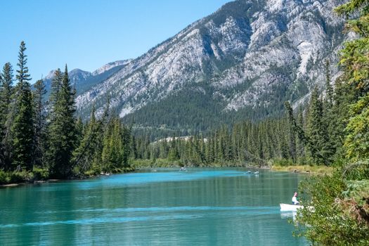 Serene scene of canoeing on a river surrounded by mountains and trees in Banff, Alberta, Canada.