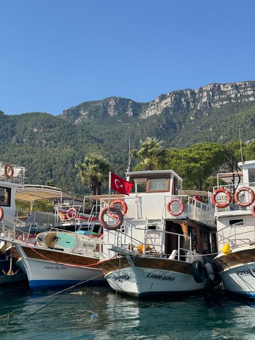 Free Colorful boats docked by a mountainside coastline in Turkey, under a clear blue sky. Stock Photo