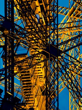 Close-up of industrial steel beams illuminated in gold, set against a clear blue sky.