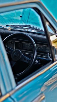 Close-up of a classic car's interior focusing on the vintage steering wheel and dashboard.