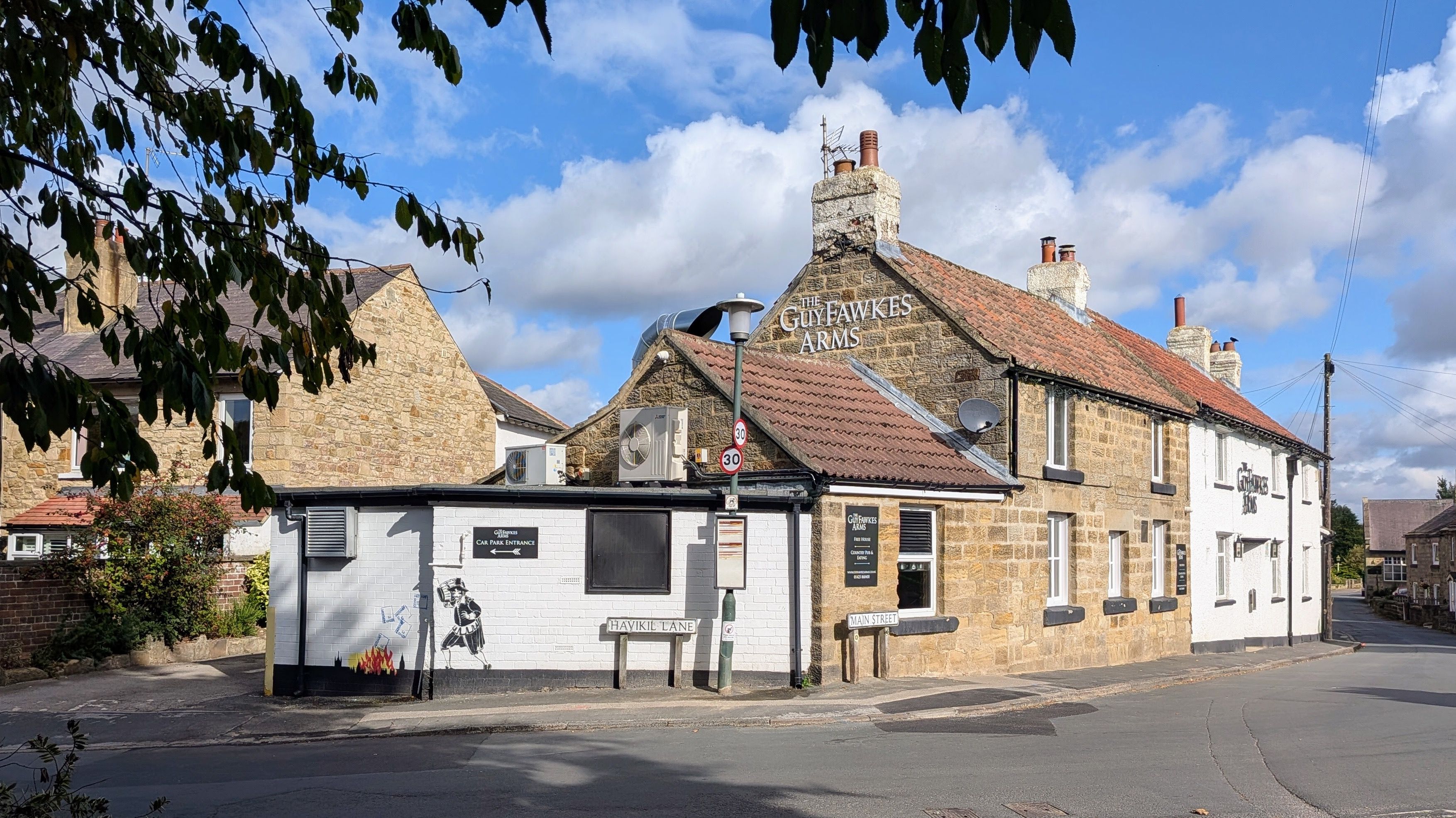 Charming exterior of The Guy Fawkes Arms pub in Scotton, England captured under a blue sky.