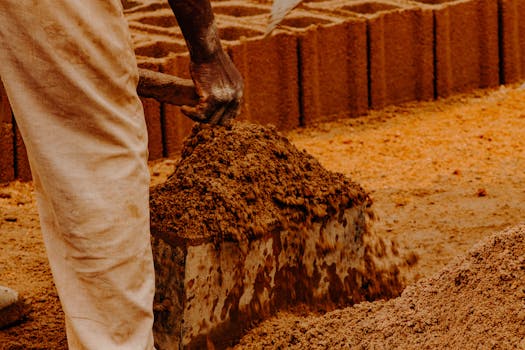 A worker shaping clay to mold bricks outdoors under natural sunlight.