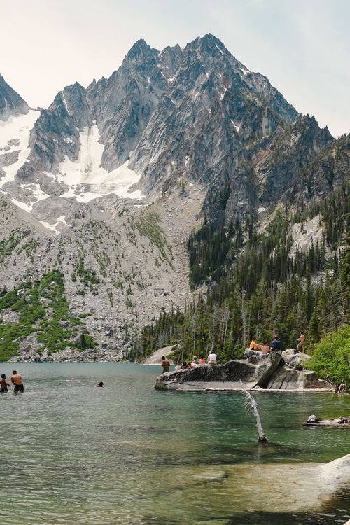 Free A picturesque mountain lake with people enjoying swimming and nature in a tranquil setting. Stock Photo