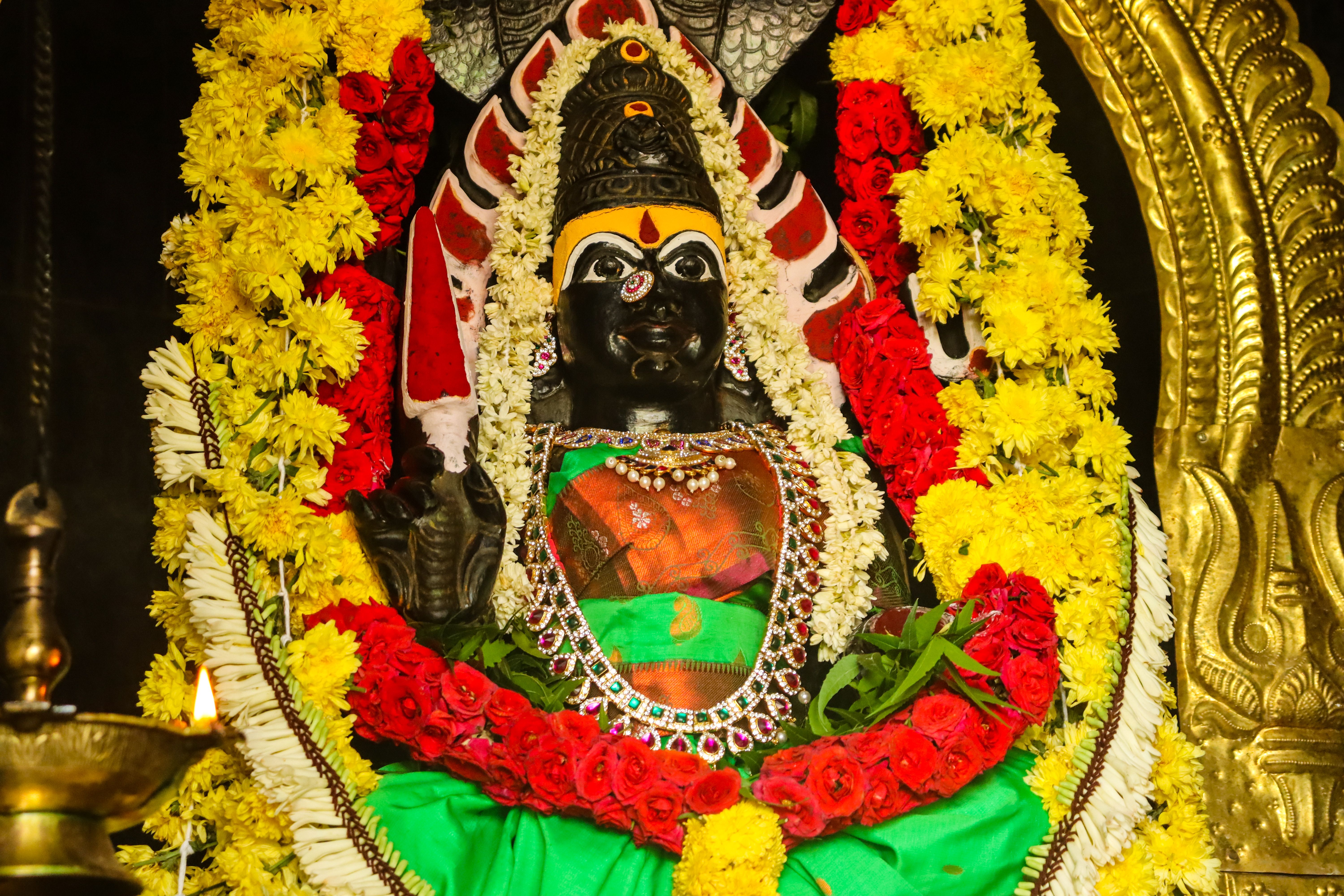 Vibrant statue of Hindu deity adorned with ornate jewelry and floral garlands in a temple setting.
