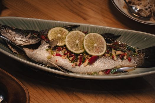 Steamed fish with lime slices and spices in a ceramic dish, perfect for Asian cuisine lovers.
