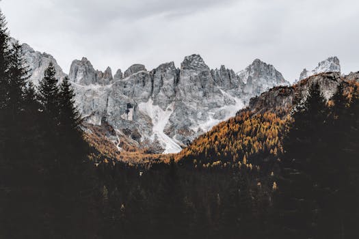 Stunning view of Dolomite mountains with autumn foliage under a cloudy sky.