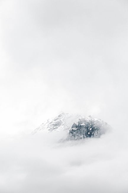 A snow-capped mountain peak emerging through dense fog, creating a serene winter landscape.