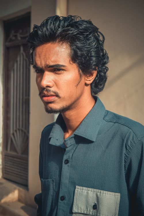 Free Portrait of a young man with curly hair standing outdoors in casual attire, exhibiting a thoughtful expression. Stock Photo
