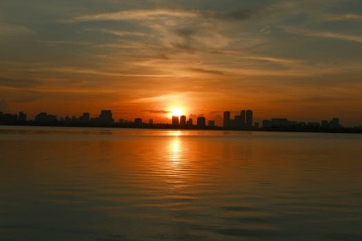 Silhouette of a city skyline against a stunning sunset over calm waters, exuding tranquility.