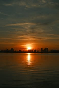 A vivid sunset over a city skyline reflecting perfectly on calm water.