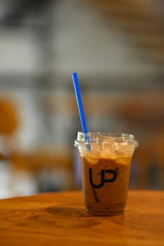 Refreshing iced coffee in a clear plastic cup with blue straw on wooden table. Perfect for caffeine lovers.