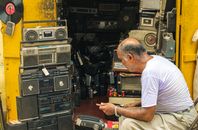 Man inspecting vintage electronics and retro radios in cluttered shop full of antique audio equipment.