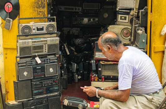 Man inspecting vintage electronics and retro radios in cluttered shop full of antique audio equipment.