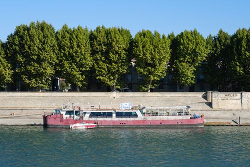 Free A vibrant riverboat docked along the Rhône in Arles, surrounded by lush trees in the summer sun. Stock Photo