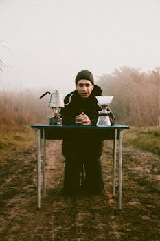 一个有雾的日子里，一名男子在户外的桌子前跪着煮咖啡，营造出一种宁静的氛围