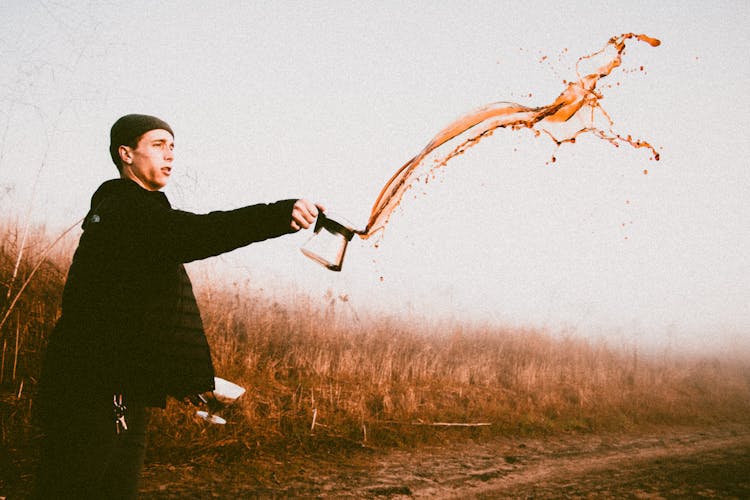 Man Throwing A Coffee By Grass Field