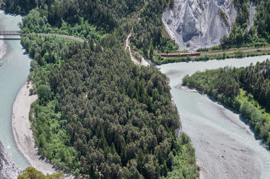 Best Private Helicopter Tour to Jura and Seeland - A Beautiful Sightseeing Flight Review Review 2026 - Scenic aerial view of the Rhine Gorge, Switzerland, showcasing lush forests, rivers, and a bright red train winding through the mountains.