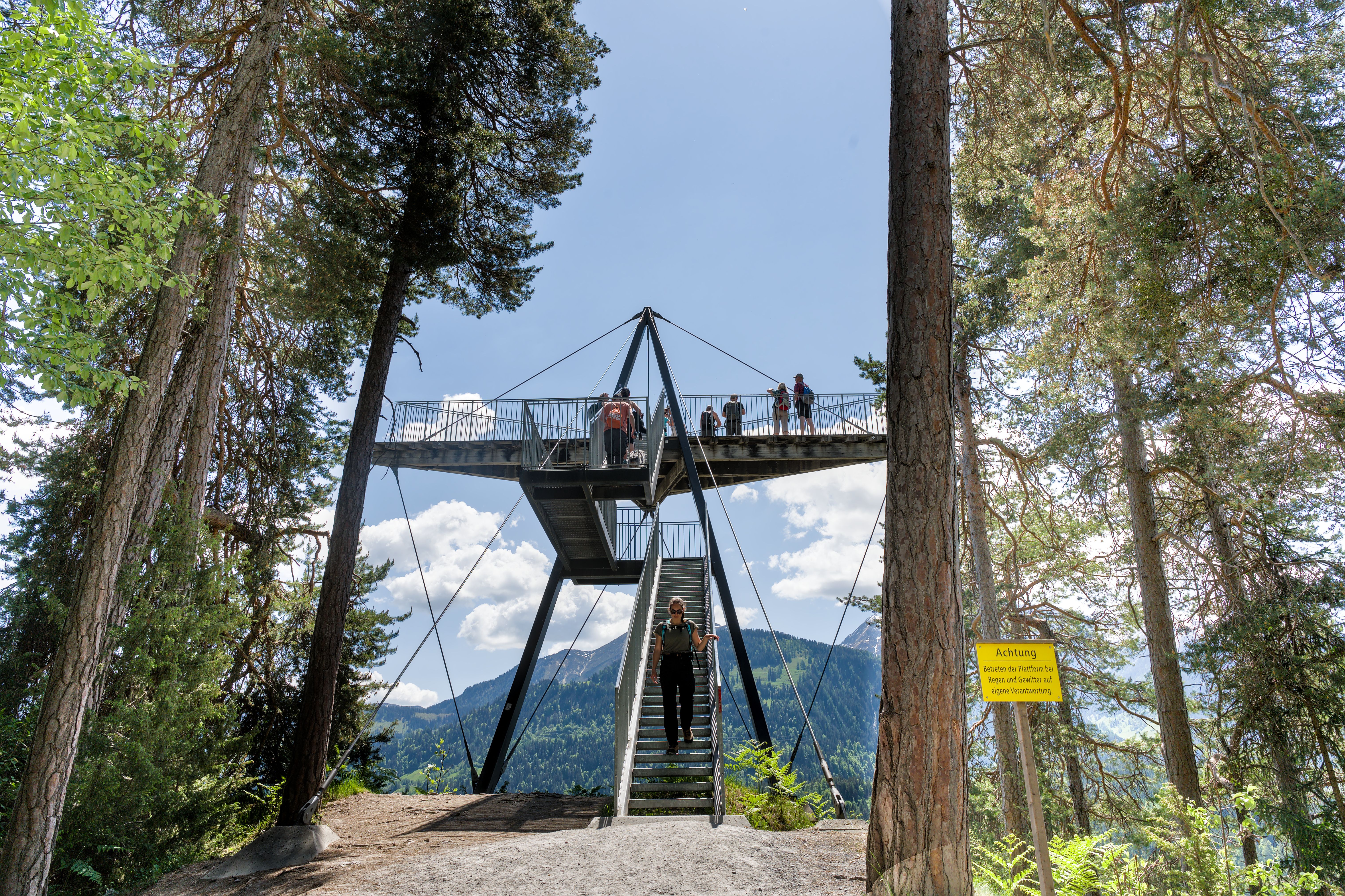 Stunning platform in Swiss forest offering panoramic mountain views, under a clear blue sky.