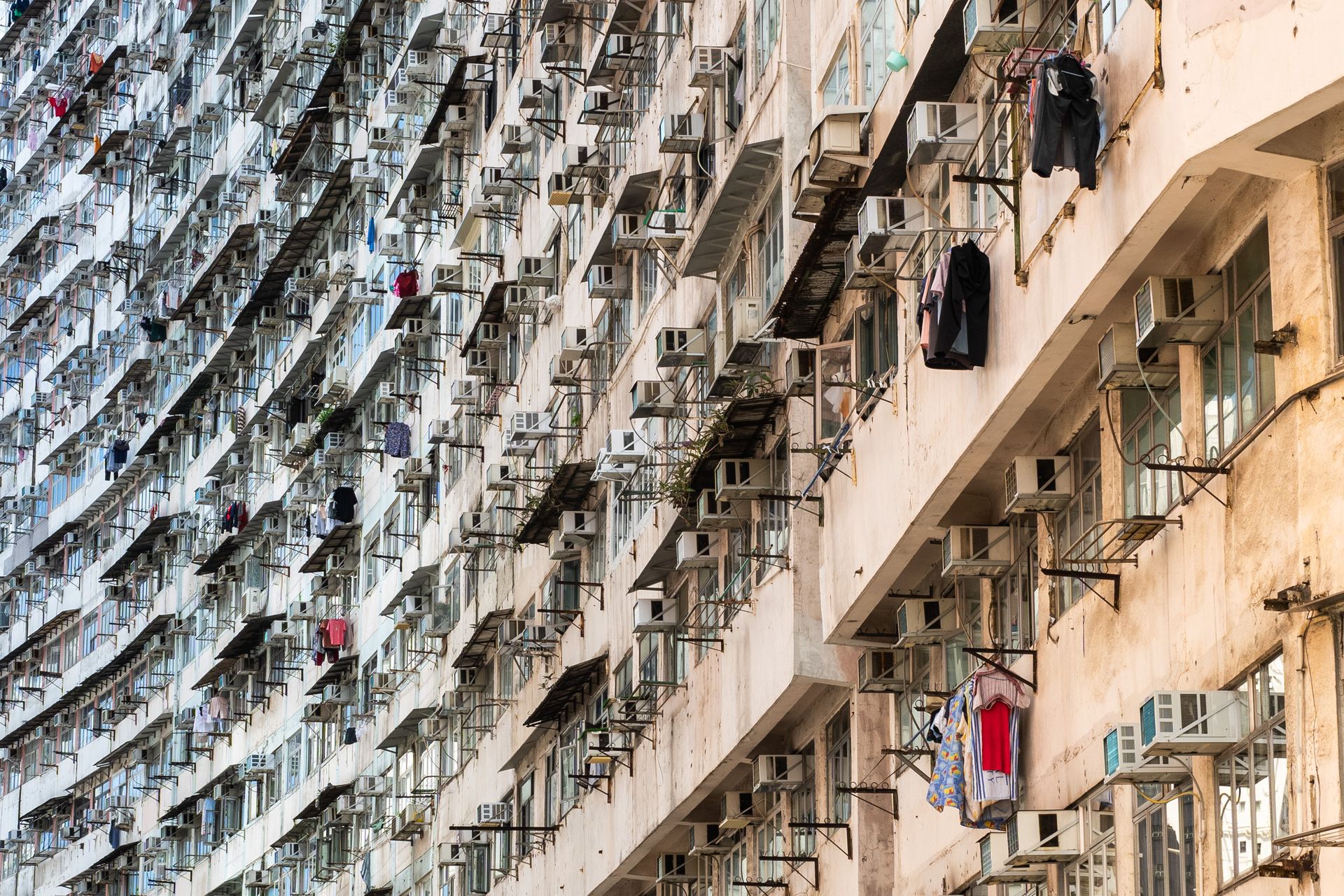Facade of a high-rise apartment complex with numerous air conditioners and hanging laundry, urban lifestyle focused.
