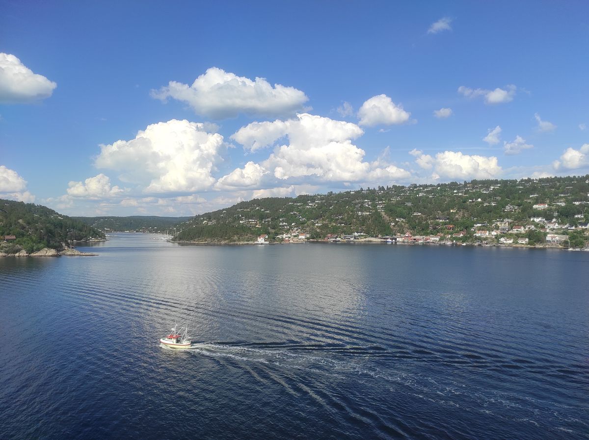 Tranquil Oslofjord with a lone boat and scenic hills under clear blue sky