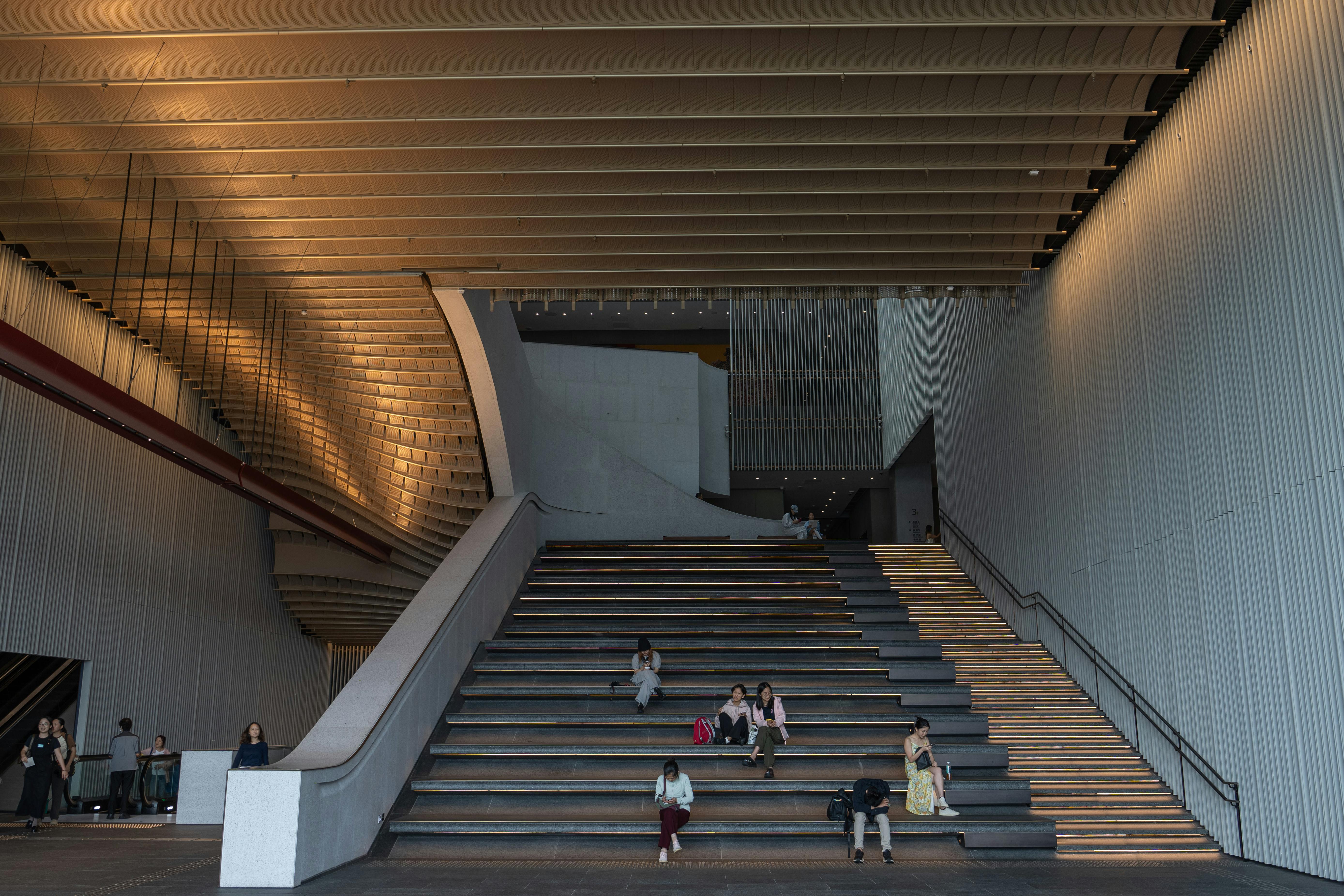 アンビエント照明と階段に座る人々を備えた現代的な室内階段は、現代建築を展示しています。