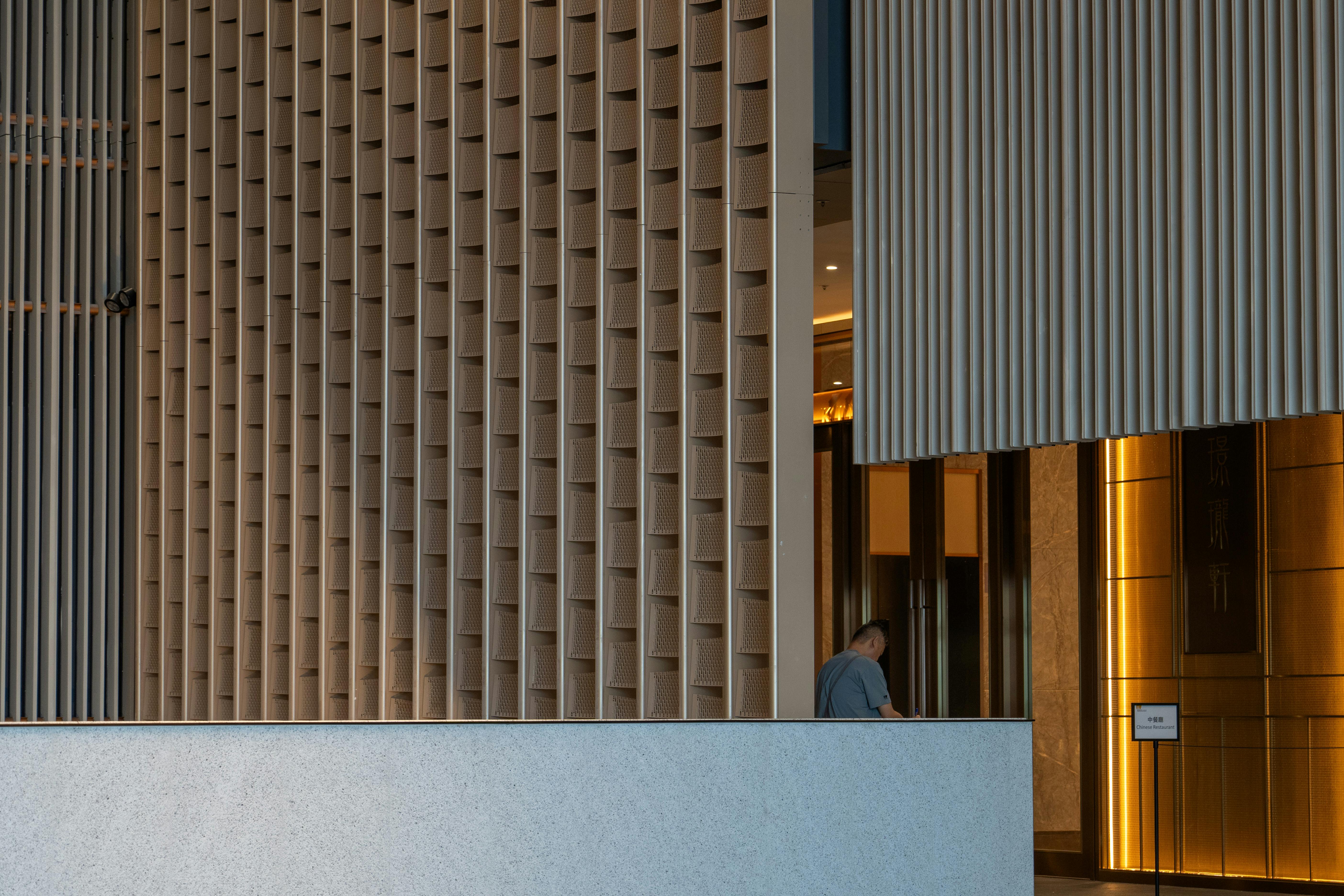 무료 수직형 목재 패널과 따뜻한 조명을 갖춘 현대적인 사무실 로비에는 성인 남성 한 명이 앉아 있습니다. 스톡 사진