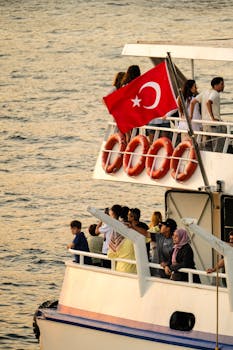 Passengers enjoy a ferry ride in Istanbul during sunset, with the Turkish flag waving above.