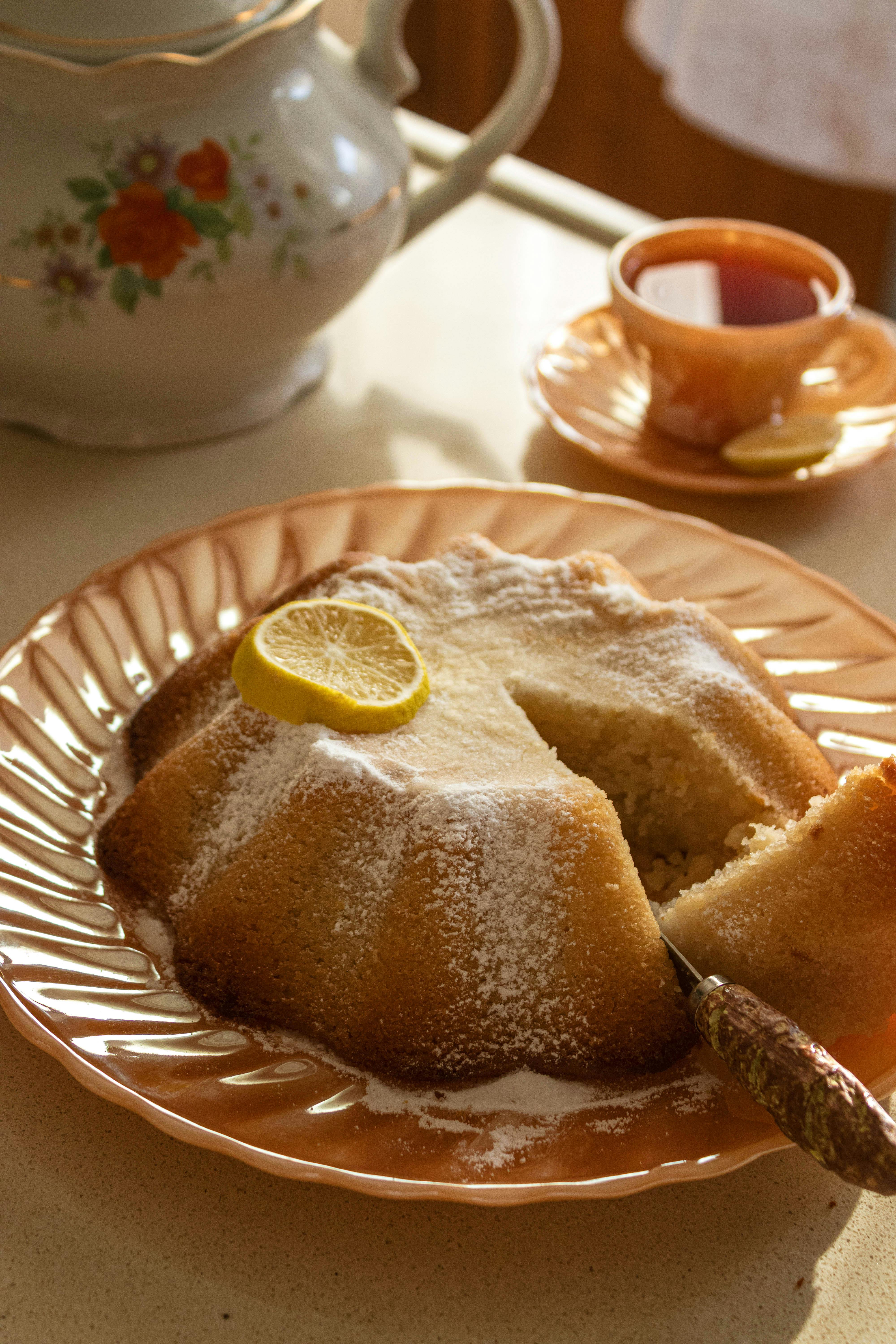 A freshly baked lemon sponge cake with a tea set on a sunny table setting.