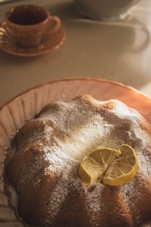 Free A sugar-dusted lemon Bundt cake with sliced lemons in a cozy tea setting. Stock Photo