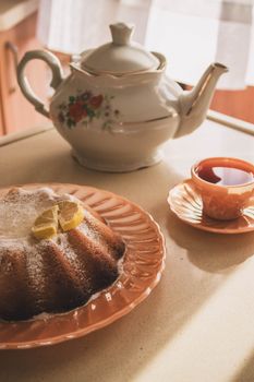 Warm sunlight illuminates a floral teapot, lemon bundt cake, and cup of tea on a cozy afternoon.