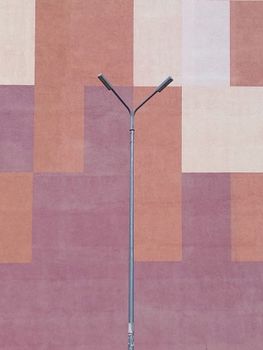 Y-shaped street lamp against a geometric colorful wall in urban setting.