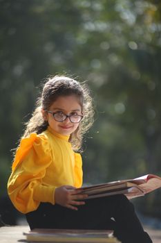 Portrait of a young girl in glasses reading outdoors, Dewas, India.