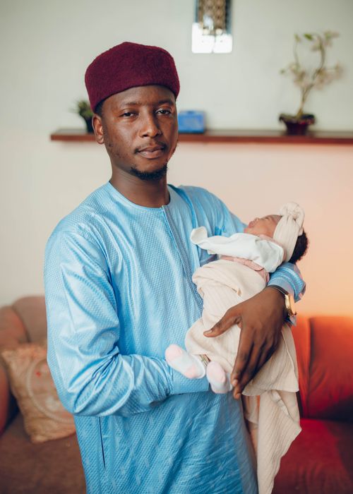 Free A Nigerian father in traditional clothing proudly holds his newborn baby indoors, showcasing cultural heritage. Stock Photo