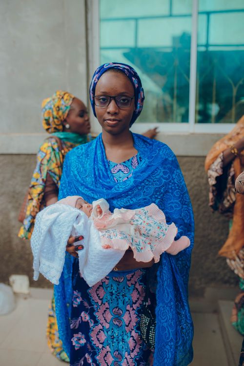 Free A Nigerian mother holds her newborn baby while wearing vibrant traditional attire outdoors. Stock Photo