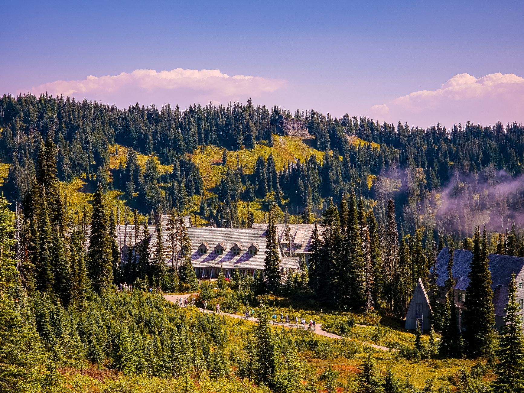 Mountain lodge nestled amidst lush evergreen forest, under vibrant blue sky.
