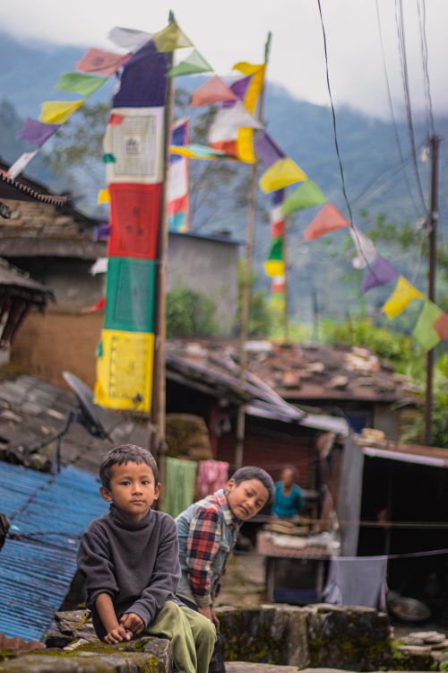 Free Two children sitting in a vibrant mountain village with colorful prayer flags above. Stock Photo