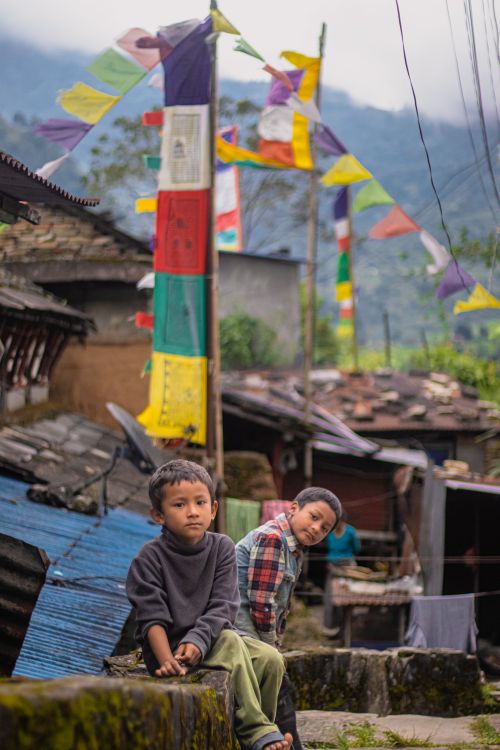 Free Two children sitting in a village with vibrant prayer flags in the background Stock Photo
