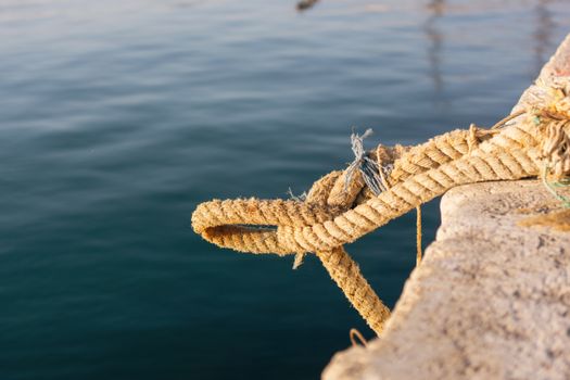 Close-up of a frayed rope on a dock with calm waters in Mersin, Türkiye.